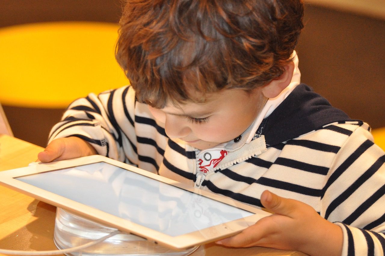 Niño pequeño mirando atentamente una tablet blanca, ideal para aplicaciones educativas y entretenimiento infantil